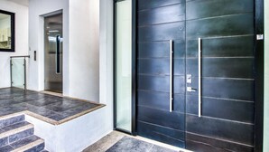 Ein moderner Eingangsbereich mit einer großen schwarzen Tür, einem Glaselevator und einer Treppe, die in eine höhere Etage führt.