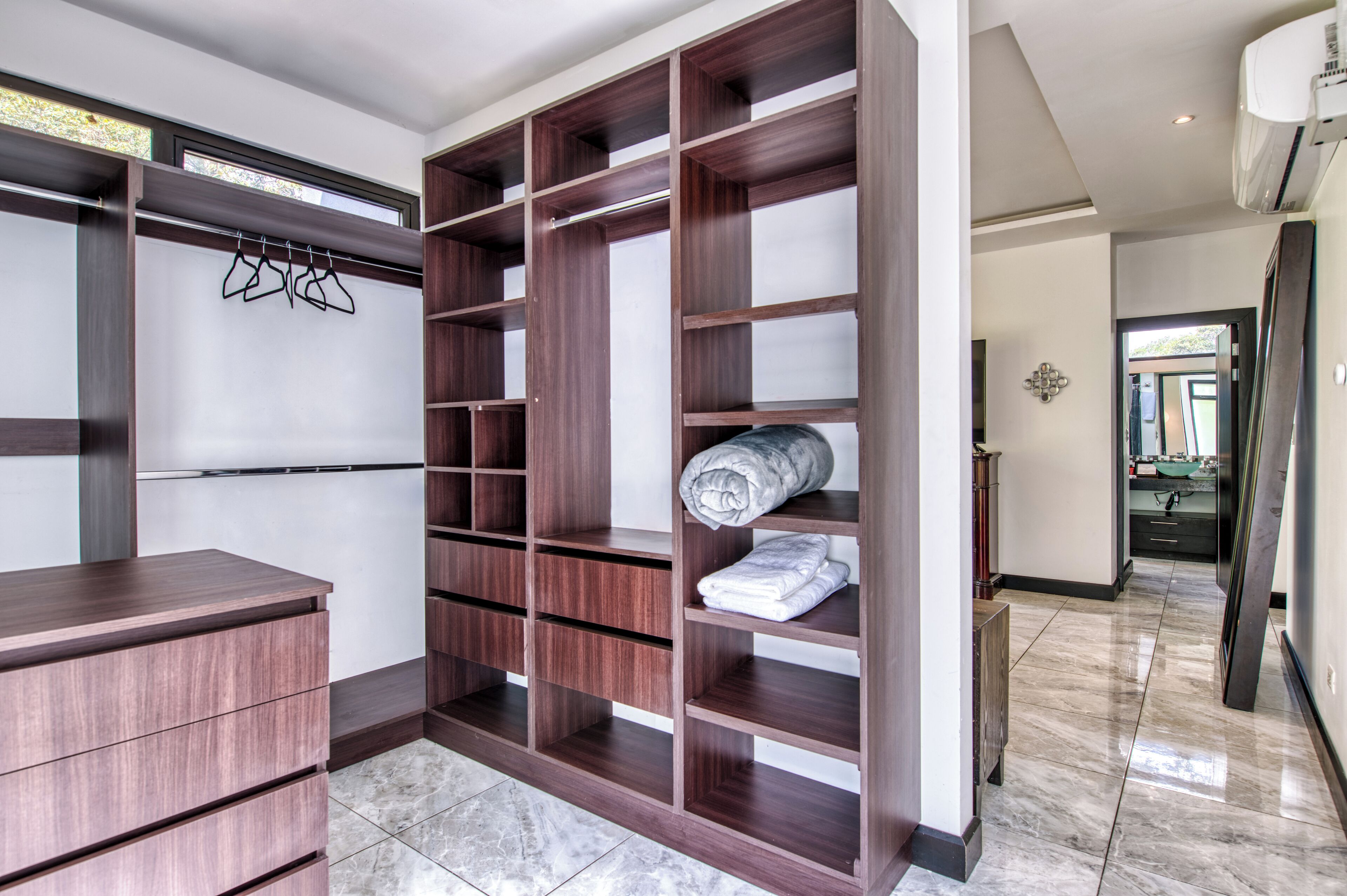A walk-in closet with wooden shelving, a built-in desk, and a marble-tiled floor.