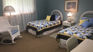 A room with two beds, a rocking chair, a small table, and a lamp.