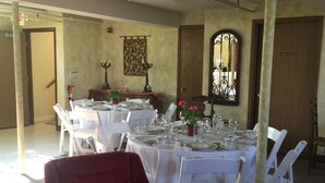 A dining area with round tables set for a meal, white chairs, and a red armchair.