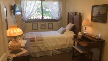 A bedroom with a bed, a desk, a lamp, a chair, a window with curtains, a picture on the wall, and a television on the wall.