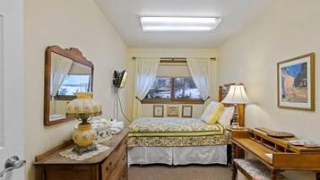 A bedroom with a bed, bedside table, lamp, dresser, and a window with curtains.