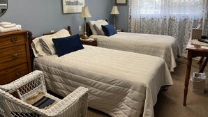 A hotel room with two beds, a wooden dresser, a wicker chair, and a window with floral curtains. - Vermilion Park Inn, #7 Spanish Room (Soudan)