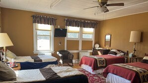 Habitación de hotel con dos camas, una silla, una mesa, una lámpara, ventilador de techo y una ventana con cortinas.