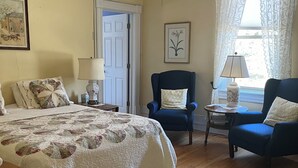 A bedroom with a large bed, two chairs, a small table, and a window with curtains. - Vermilion Park Inn, #12 Celtic Room (2nd floor) w/ensuite (Soudan)
