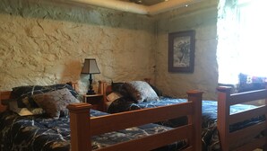 A bedroom with two wooden beds, a nightstand with a lamp, and a stone wall. - Vermilion Park Inn, LL Bear's Den ( lower level) (Soudan)