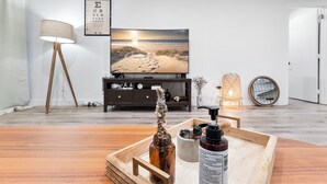 Una sala moderna con suelo de madera, un televisor de pantalla plana sobre un mueble de madera oscura, una lámpara y una planta decorativa.