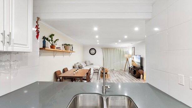 Una cocina moderna con un lavamanos doble, una mesa de comedor de madera y una sala de estar acogedora con sofá y televisor.