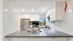 Cocina moderna con armarios blancos, electrodomésticos de acero inoxidable y una isla central con taburetes.