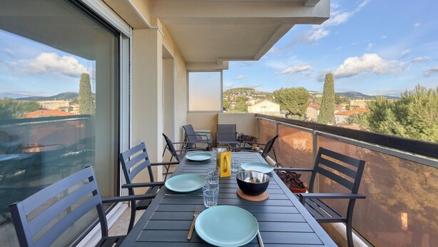 Un balcon avec une table dressée pour deux personnes, des chaises, un saladier et une plante en pot.