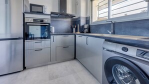 Une cuisine compacte dotée d’appareils électroménagers en acier inoxydable, d’un four encastré, d’un four à micro-ondes et d’un lave-linge.