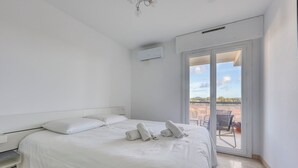 Une chambre à coucher avec un lit, deux oreillers, un mur blanc, un appareil de climatisation et une porte-fenêtre coulissante donnant sur un espace extérieur.