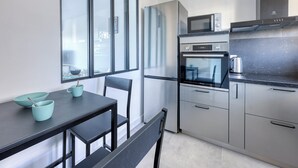 Une cuisine moderne équipée d’un réfrigérateur, d’un four, d’un four à micro-ondes et d’une machine à café. On y trouve une table à manger avec des chaises, ainsi qu’une fenêtre qui laisse entrer la lumière naturelle.