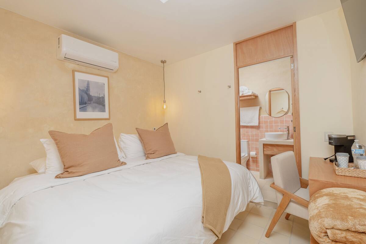 A hotel room with a bed, a desk, a chair, a sink, and a mirror.