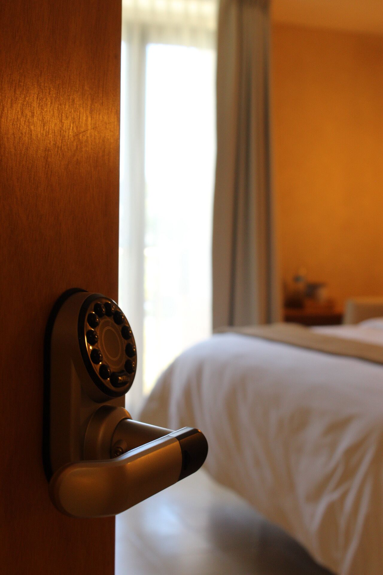 Une chambre d’hôtel avec une porte en bois, un trou de serrure et un lit recouvert de draps blancs.