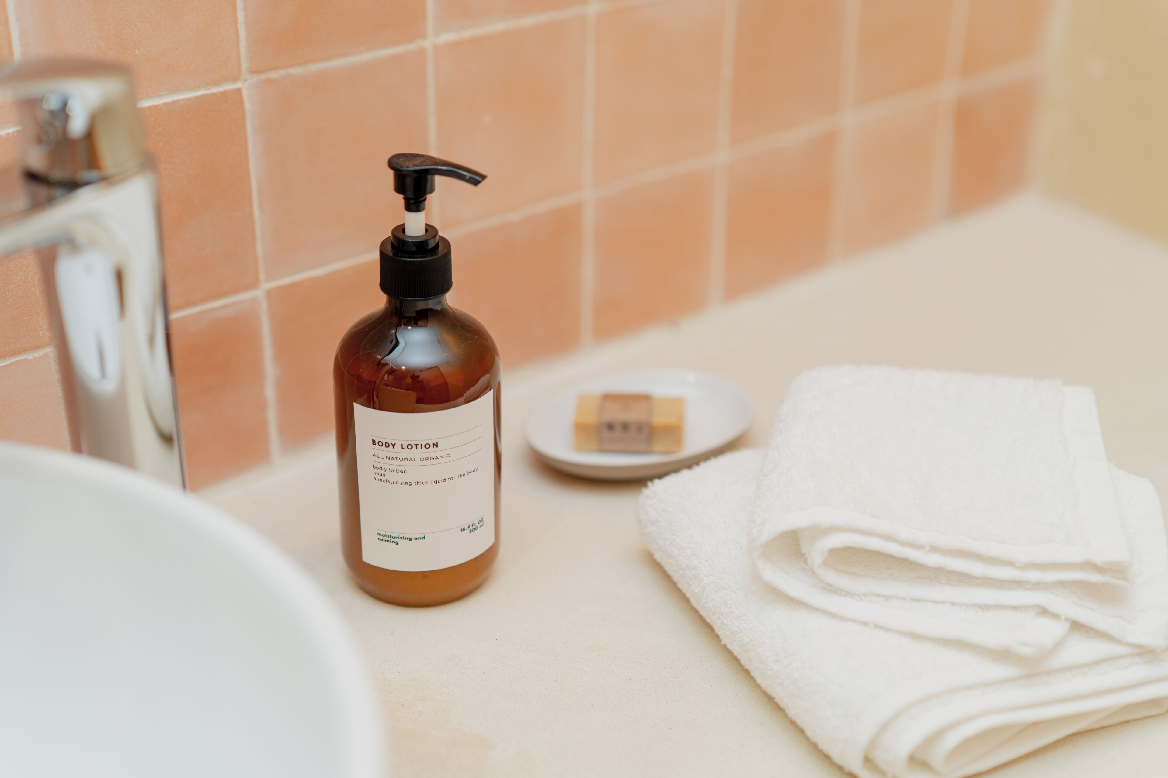 Een badkamer met een bruine lotionfles, een zeepbakje en een opgevouwen witte handdoek.