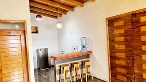 Uma cozinha com vigas de madeira, um espaço bar com banquetas, uma geladeira e um bebedouro.