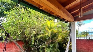 Uma rede sob um teto de madeira, com vista para um gramado verde e árvores.