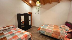 Quarto com duas camas, piso de madeira, guarda-roupa e luminária pendente.