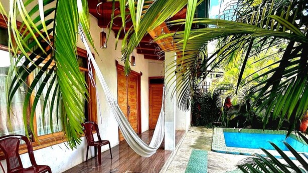 Um deck de madeira com rede, cadeiras e piscina.