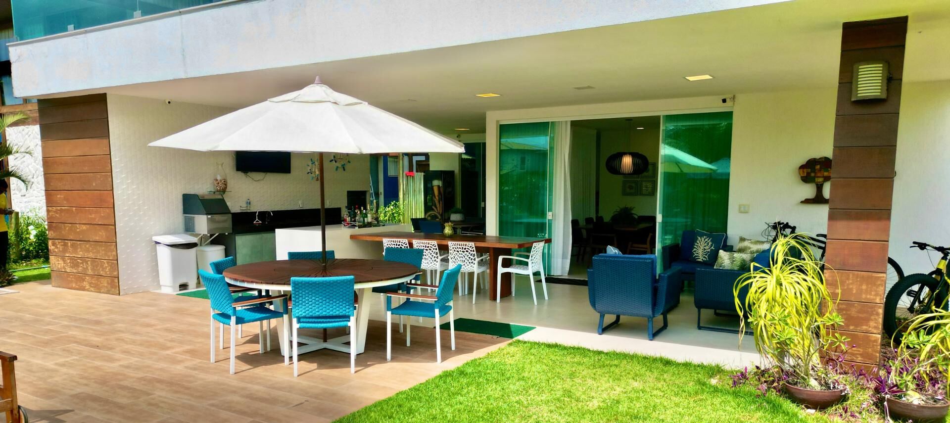 A modern outdoor dining area with a round table and chairs, a white umbrella, and a view into the house.