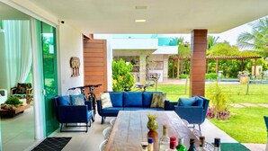 Un espacio moderno al aire libre con sofás azules y una mesa de madera, rodeado de follaje y vistas a una piscina.