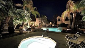 An outdoor swimming pool area at night with lounge chairs and palm trees. - Charming 3-bedroom condo with fitness room and WiFi in Scottsdale (Scottsdale)