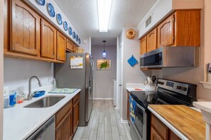 Una cocina estrecha con armarios de madera, electrodomésticos de acero inoxidable y salpicadero de azulejos.