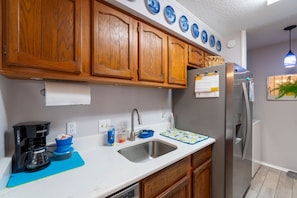 Una cocina con armarios de madera, un refrigerador de acero inoxidable, una cafetera y un lavamanos con un tapete azul.