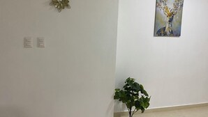 A room with a white wall, three decorative metal flowers, a painting of a deer, and a potted plant.