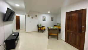 A spacious living area with a flat-screen TV mounted on the wall, a wooden door, and a dining table with chairs.