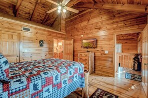 Ein gemütliches Blockhauszimmer mit Bett, Deckenventilator, Fernseher und Holztür.