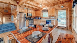 Interior de una cabaña de madera con cocina, comedor y un gran ventanal.