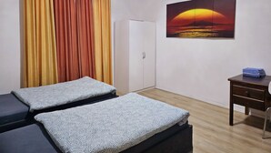 Ein Zimmer mit zwei Betten, einem Schreibtisch, einem Stuhl, einem Kleiderschrank und einem Gemälde vom Sonnenuntergang.