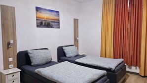 Ein Hotelzimmer mit zwei Betten, einem Nachttisch, einer Wandleuchte und einem Sonnenuntergangsbild.