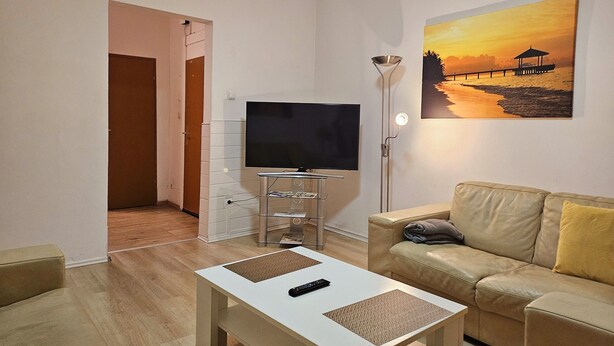 Ein Wohnzimmer mit Flachbildfernseher auf einem Standfuß, einer Couch, einem Couchtisch und einem Sonnenuntergangsbild an der Wand.