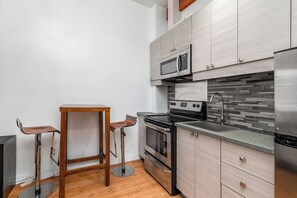 Cocina compacta con microondas, estufa y refrigerador, que presenta gabinetes de madera y salpicadero de azulejos.