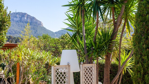 A garden with a white lamp post, a wooden fence, and a mountain in the background. - Apartment 'Le Repaire' with Mountain View, Shared Terrace and Garden (Cassis)