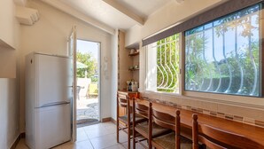 A kitchen with a refrigerator, wooden dining table, chairs, and a window with a view of greenery. - Apartment 'Le Repaire' with Mountain View, Shared Terrace and Garden (Cassis)