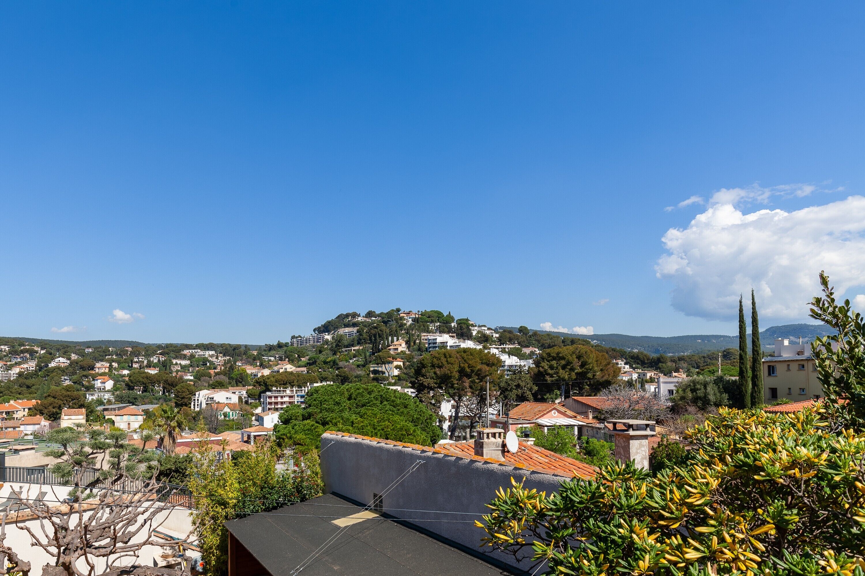 Un quartier résidentiel avec des maisons, une colline parsemée de bâtiments et un ciel bleu dégagé.