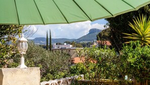 A patio area with a green umbrella, a white lamp, and a view of a mountainous landscape. - Apartment 'Le Repaire' with Mountain View, Shared Terrace and Garden (Cassis)