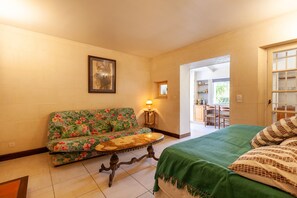 A room with a floral sofa, a small table, a bed with a green bedspread, and a framed picture on the wall.