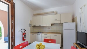 Una cocina compacta con una mesa blanca, un plato de limones, un refrigerador blanco y una silla roja.
