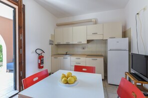 A compact kitchen with a white table, a plate of lemons, a white refrigerator, and a red chair.