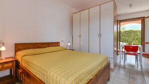 Un dormitorio con cama, armario, escritorio con lámpara y vista a zonas verdes.