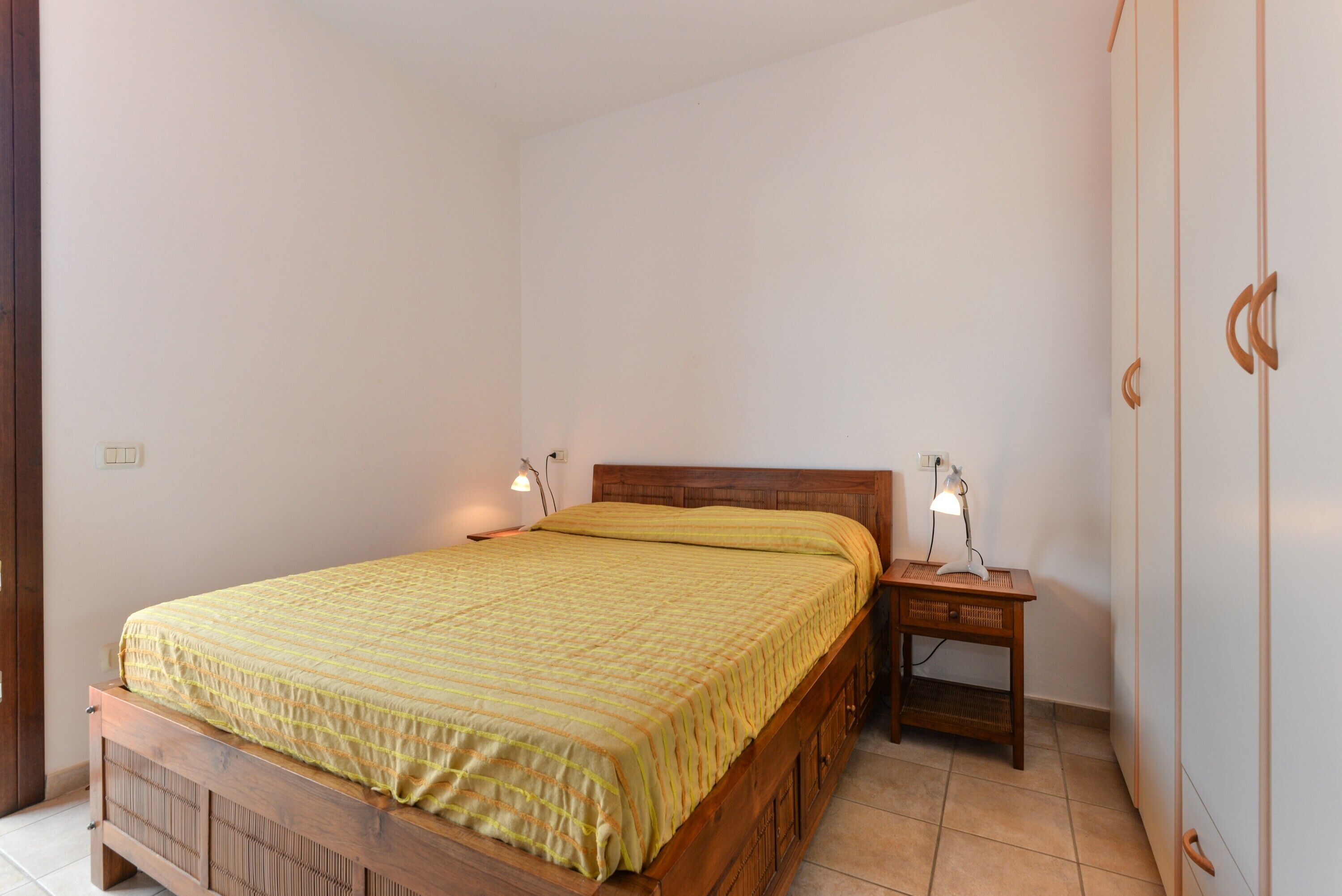 A bedroom with a wooden bed, two bedside lamps, a nightstand, and a wardrobe.