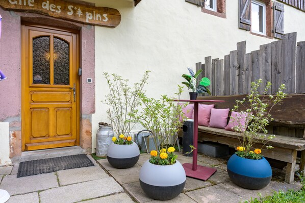 A wooden door, a bench, and three large planters with flowers.