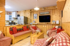 A cozy wooden interior with a sofa set, a television, and a kitchen area.
