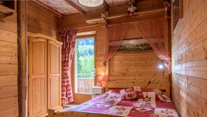 A wooden cabin bedroom with a bed, a wardrobe, a window with curtains, and a small table with a lamp. - Apartment 'Des Sapins' with Mountain View, Private Terrace and Wi-Fi (La Bresse, Grand Est, France)