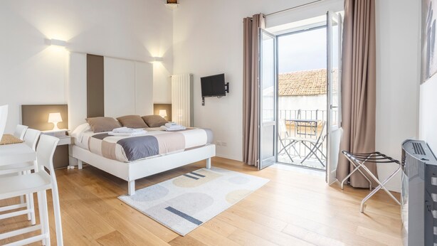 A bedroom with a bed, bedside table, lamp, TV, and a view of the outside. - Apartment 'Melo' with Balcony, Wi-Fi and Air Conditioning (Palermo)